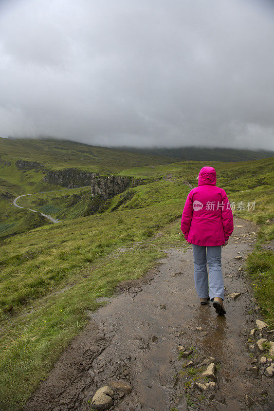 在苏格兰Skye岛的cuith - raining山脉上，一位资深女性徒步旅行者身后的景色，通常被称为Quiraing。